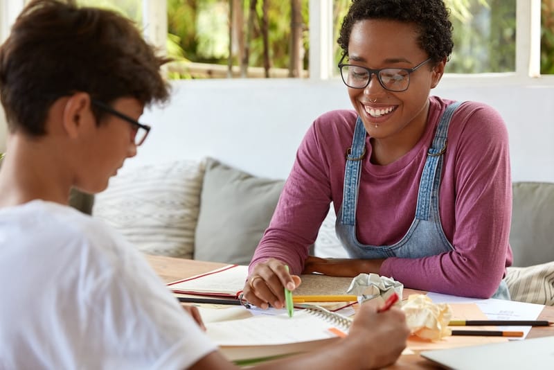 A tutor working one-on-one with a student at a table, reviewing written work together